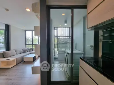 Modern apartment with sleek kitchen and laundry area, featuring large windows and stylish living room.