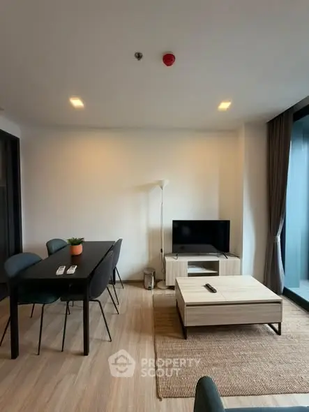 Modern living room with dining area and TV, featuring sleek furniture and natural light.