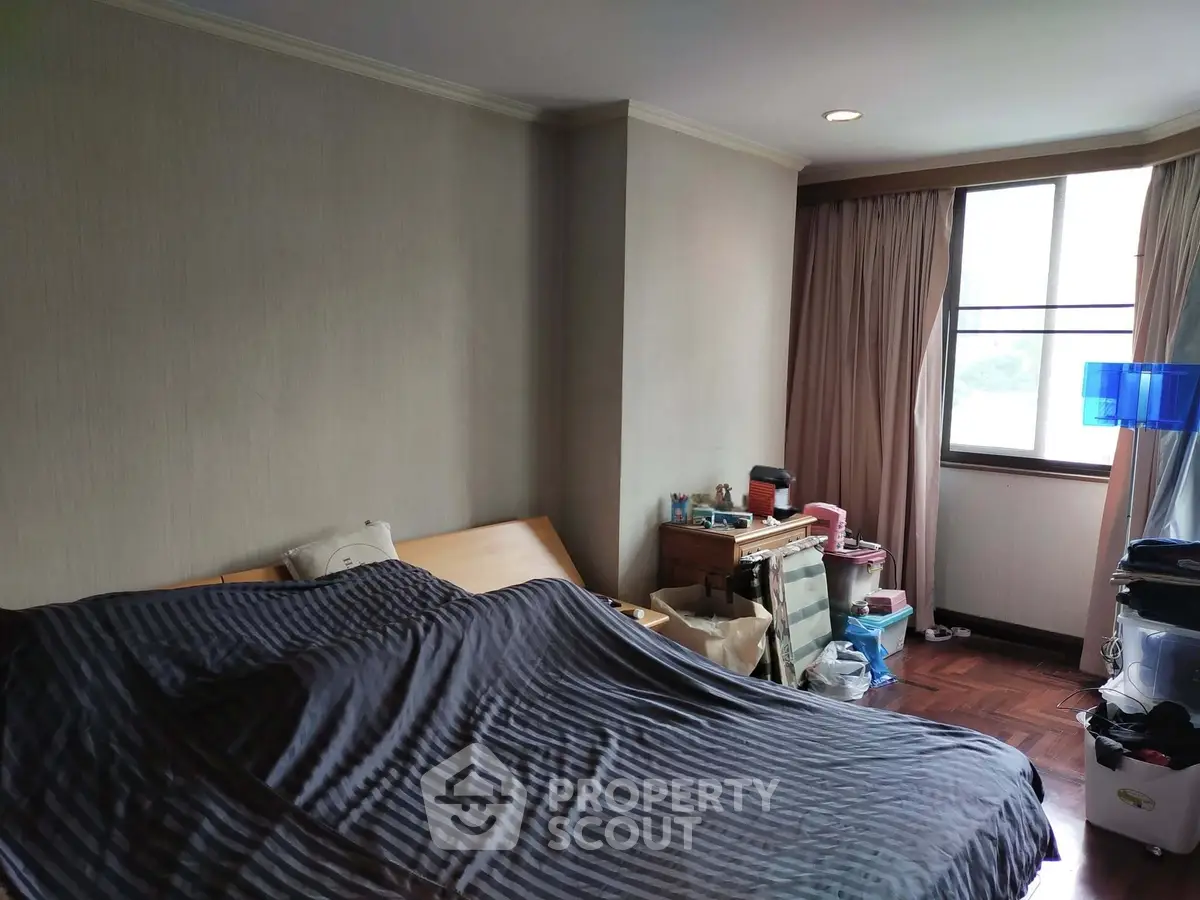 Spacious bedroom with large window and cozy furnishings in a modern apartment.