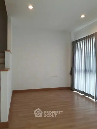 Spacious empty room with wooden flooring and large window with curtains, ideal for customization.