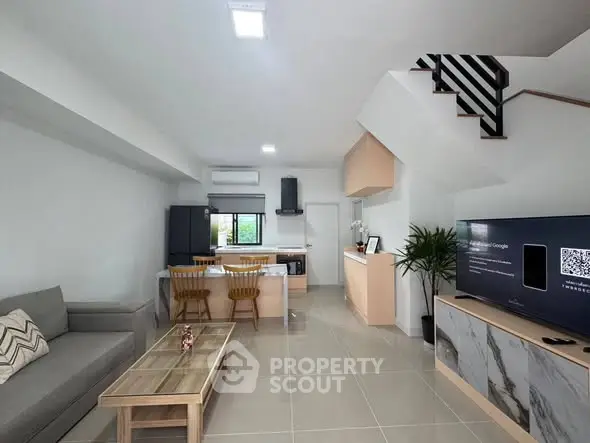Modern open-plan living room with kitchen and staircase, featuring sleek furniture and natural light.