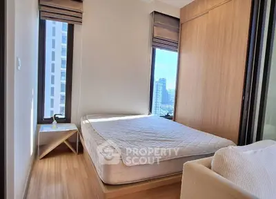 Modern bedroom with large windows and city view, featuring a cozy bed and wooden flooring.