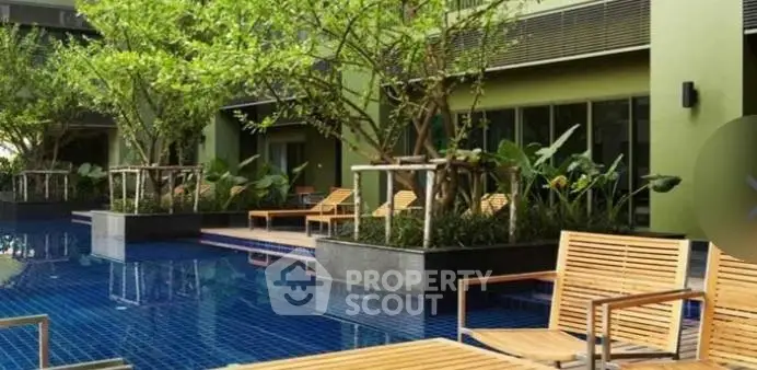 Luxurious outdoor pool area with lush greenery and stylish wooden loungers in a modern residential complex.