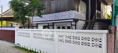 Charming two-story home with decorative balcony and lush greenery, perfect for serene living.