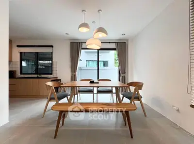 Modern dining area with wooden table and chairs, open layout kitchen, and large windows.