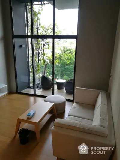 Serene living room with floor-to-ceiling windows offering a lush garden view, complemented by modern minimalist furniture.