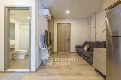 Modern living room with wooden flooring and open view to bathroom, featuring sleek furniture and appliances.
