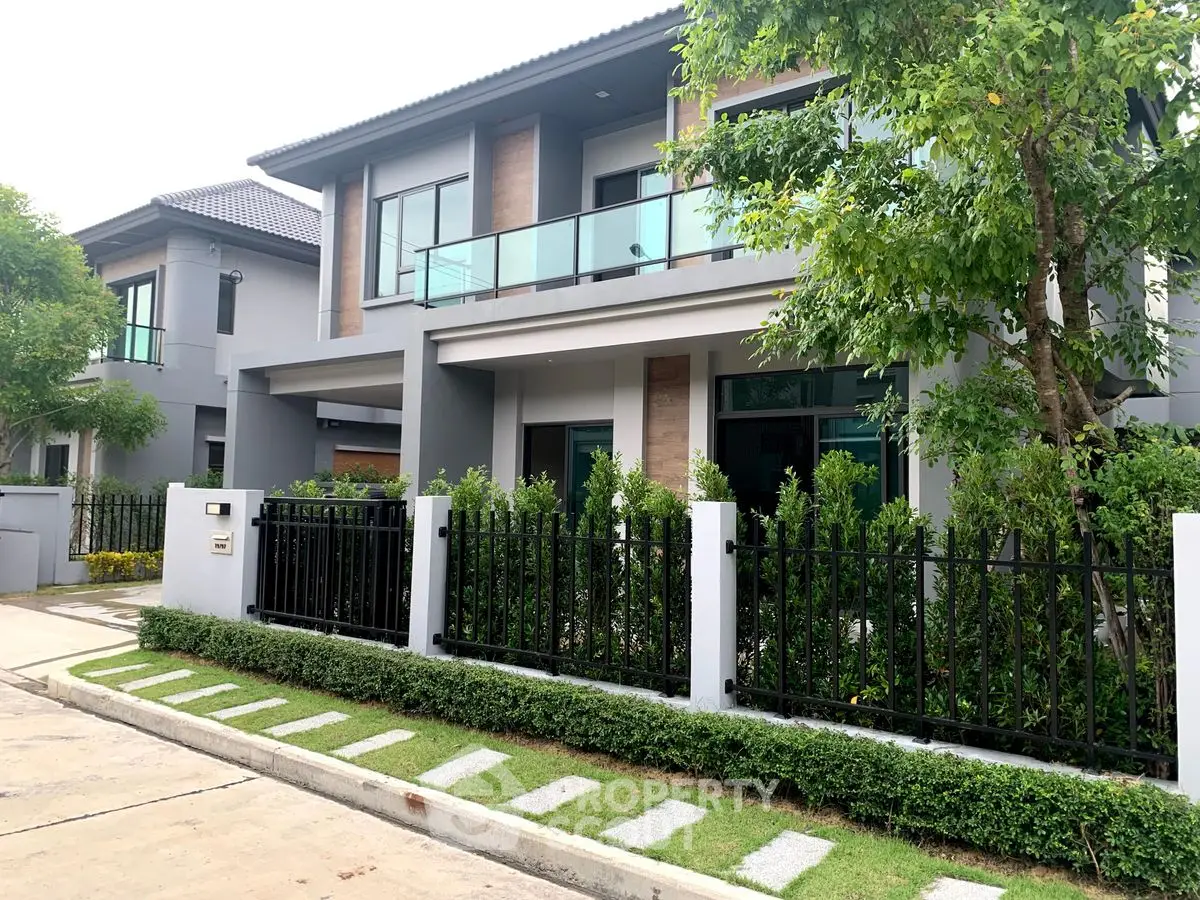 Modern two-story house with lush garden and sleek fence in suburban neighborhood.