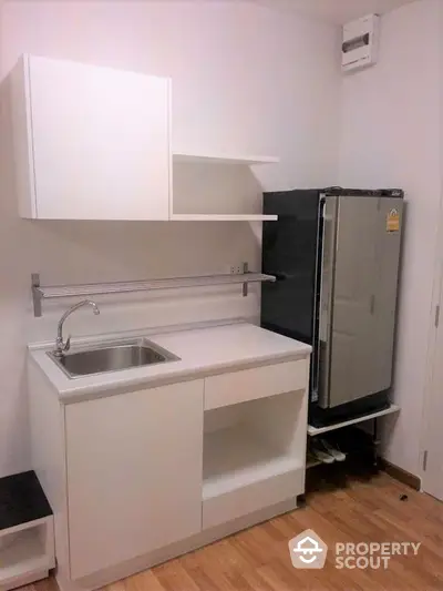 Modern compact kitchen with sleek white cabinets and stainless steel fridge