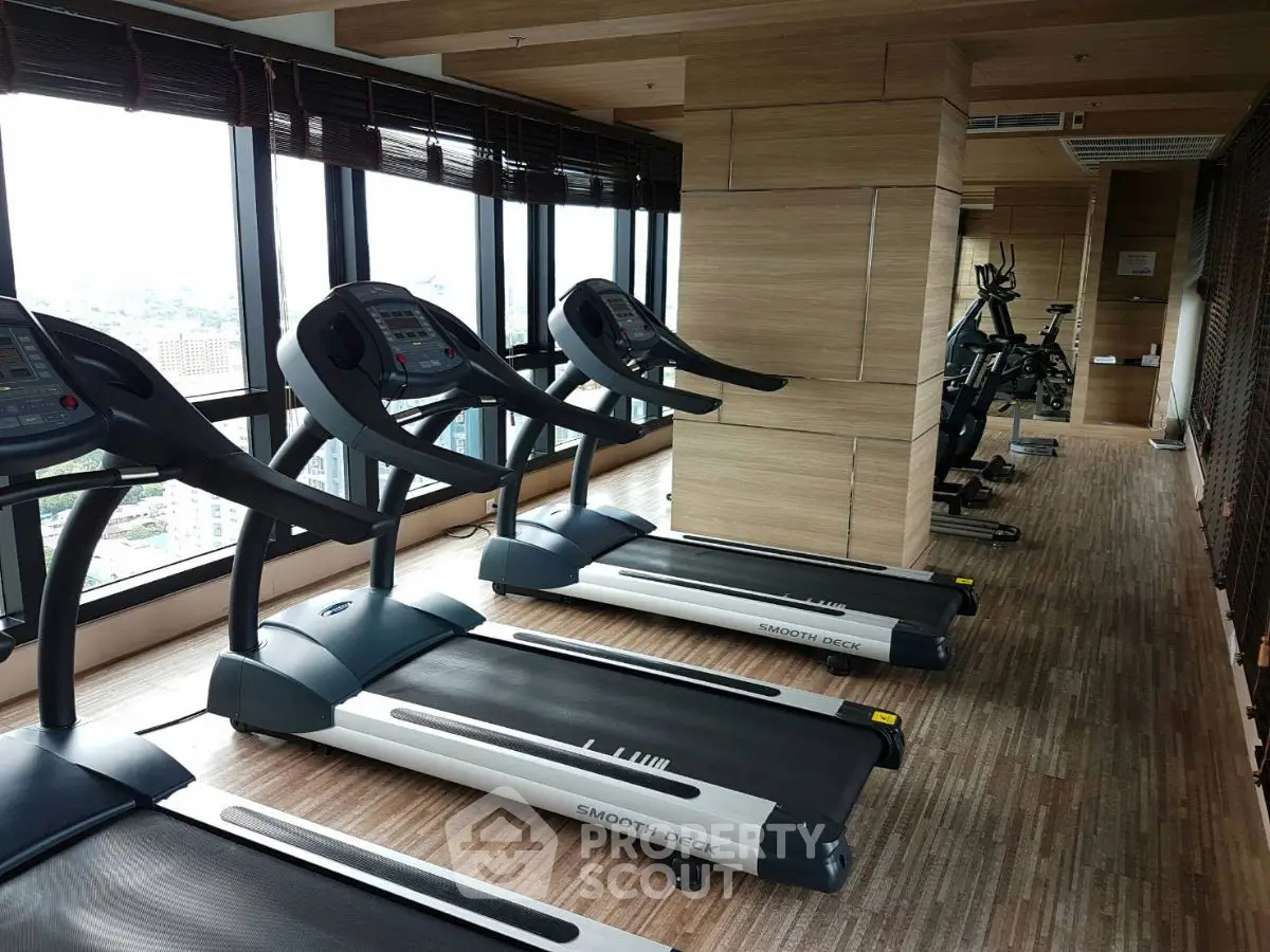 Spacious gym with modern treadmills and city view in luxury apartment building.