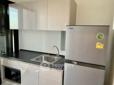 Modern kitchen with sleek cabinets, stainless steel fridge, and built-in microwave.