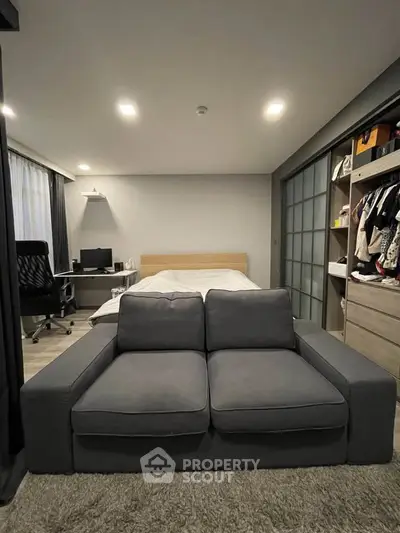 Modern bedroom with cozy sofa, workspace, and stylish wardrobe in a compact layout.