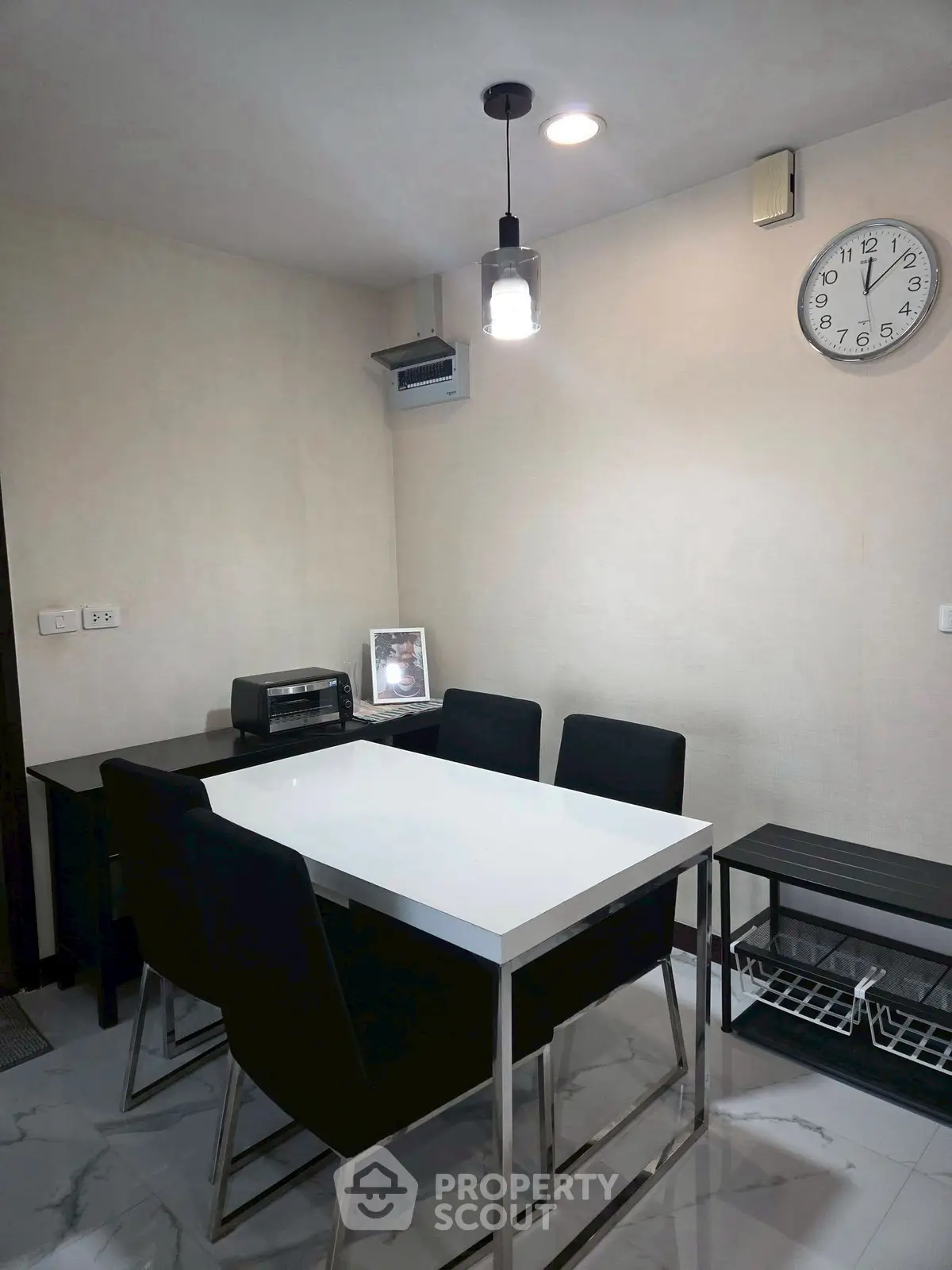 Modern dining area with sleek black chairs and white table, featuring a wall clock and minimalist decor.