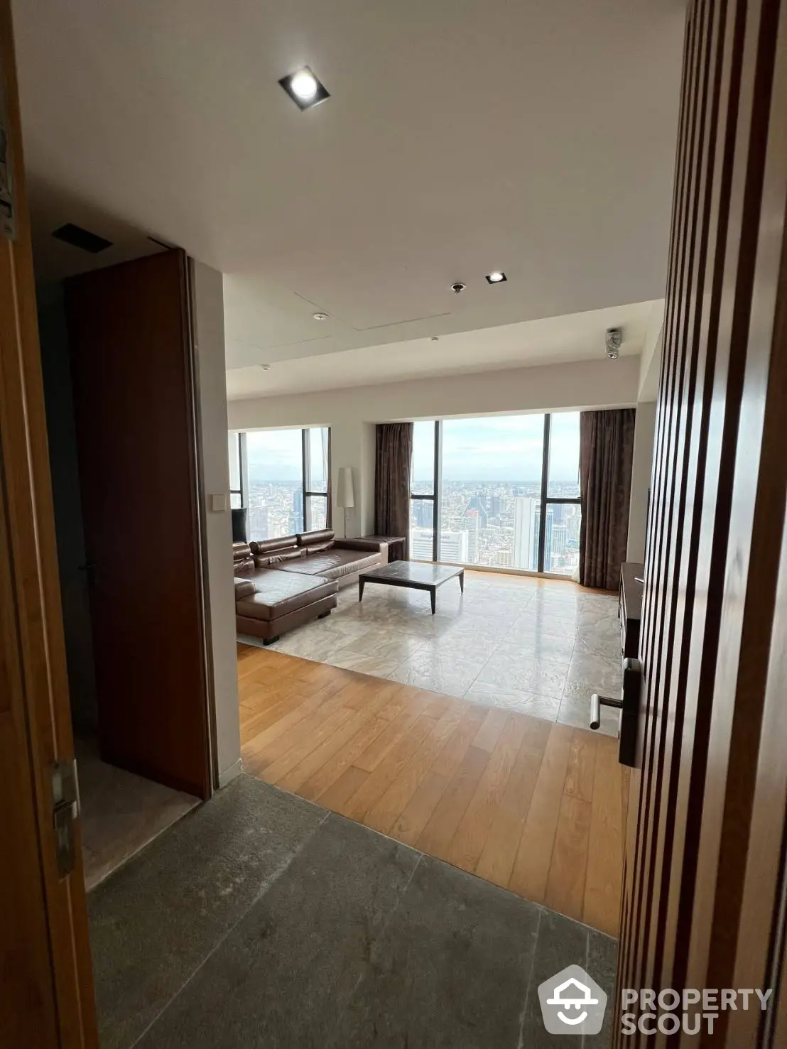 Expansive high-rise living room with floor-to-ceiling windows offering a panoramic city view, elegant wooden flooring, and modern lighting.