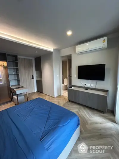 Modern bedroom with sleek design, featuring a blue bedspread, wall-mounted TV, and air conditioning.