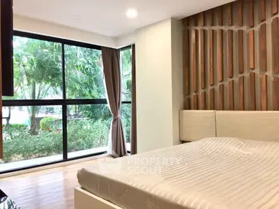 Spacious bedroom with large windows and garden view, featuring modern decor and natural light.
