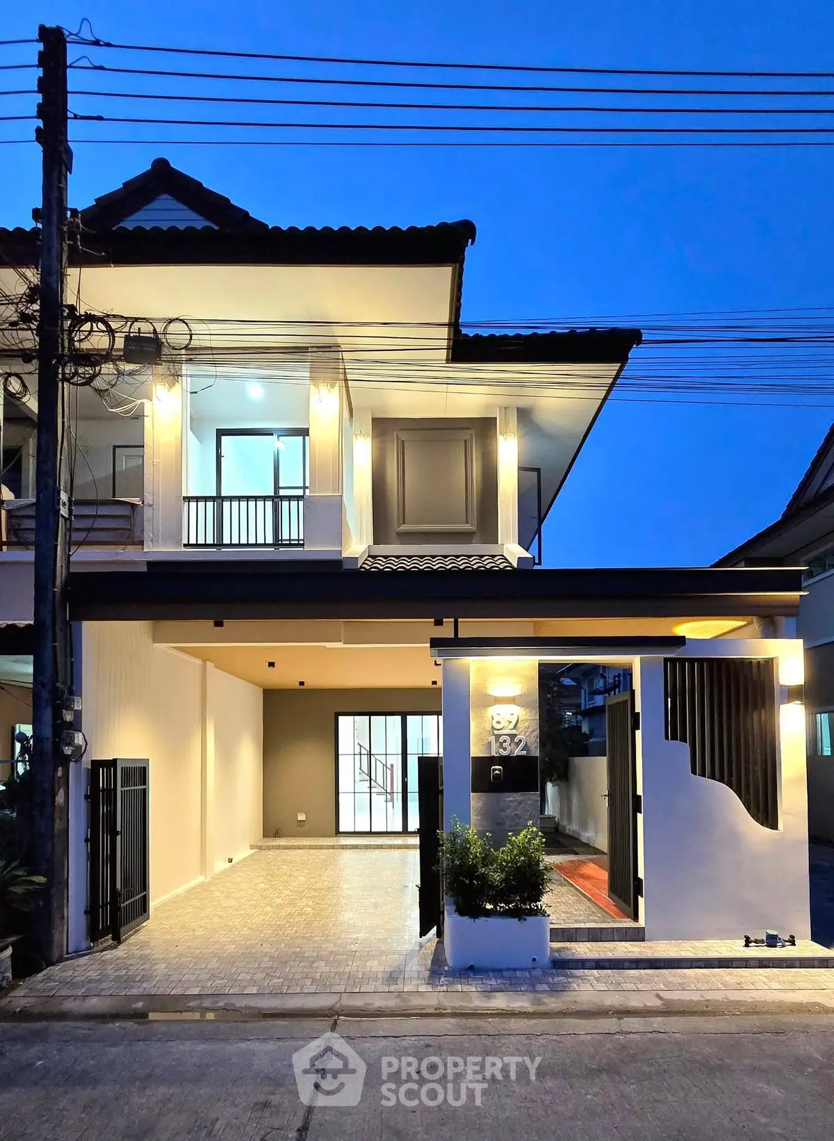 Modern two-story house with stylish exterior lighting and spacious carport at dusk.