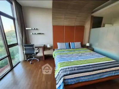 Modern bedroom with large window and stylish decor, featuring a cozy workspace.