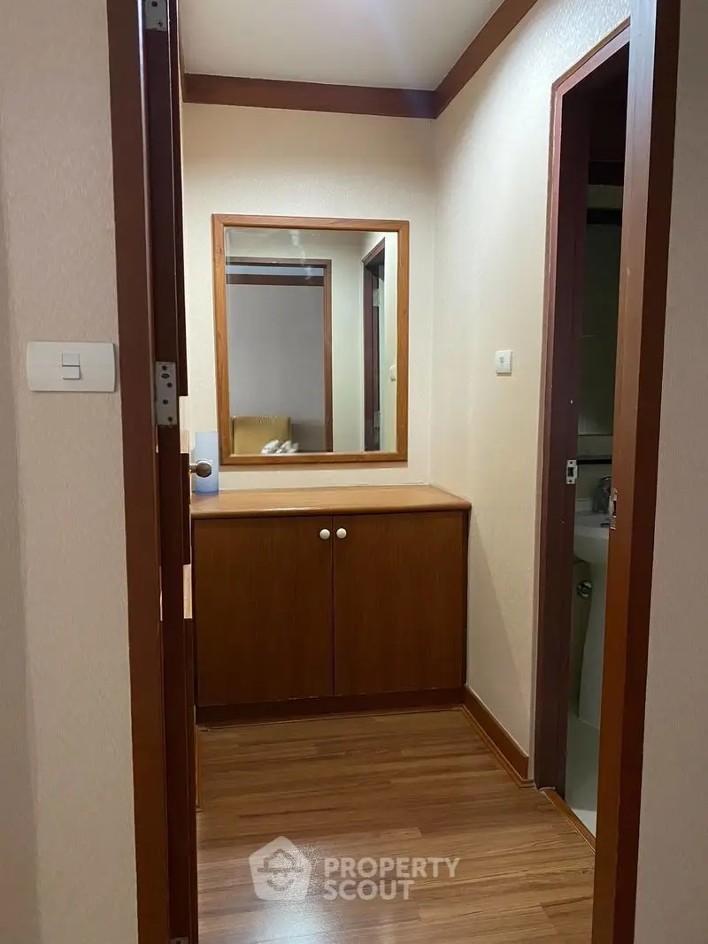 Cozy hallway with wooden flooring and built-in cabinet, leading to a bathroom.