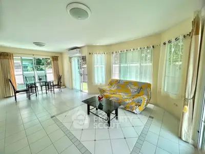 Spacious living room with large windows and garden view, featuring modern furniture and tiled flooring.