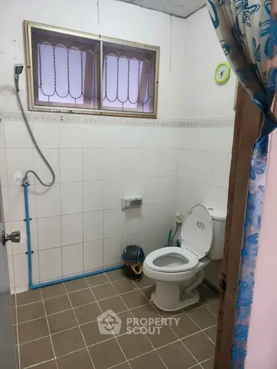Simple bathroom with tiled walls and floor, featuring a toilet and shower area.