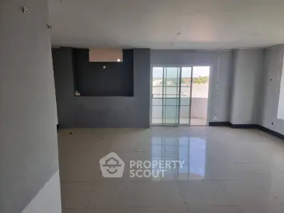 Spacious unfurnished living room with large windows and balcony access, offering ample natural light.