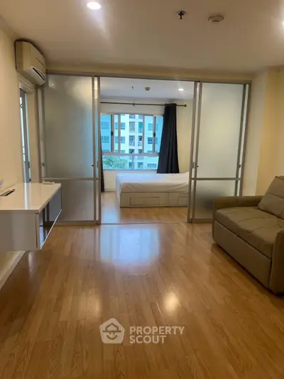 Spacious studio apartment with modern sliding glass doors and wooden flooring, offering a cozy living space.