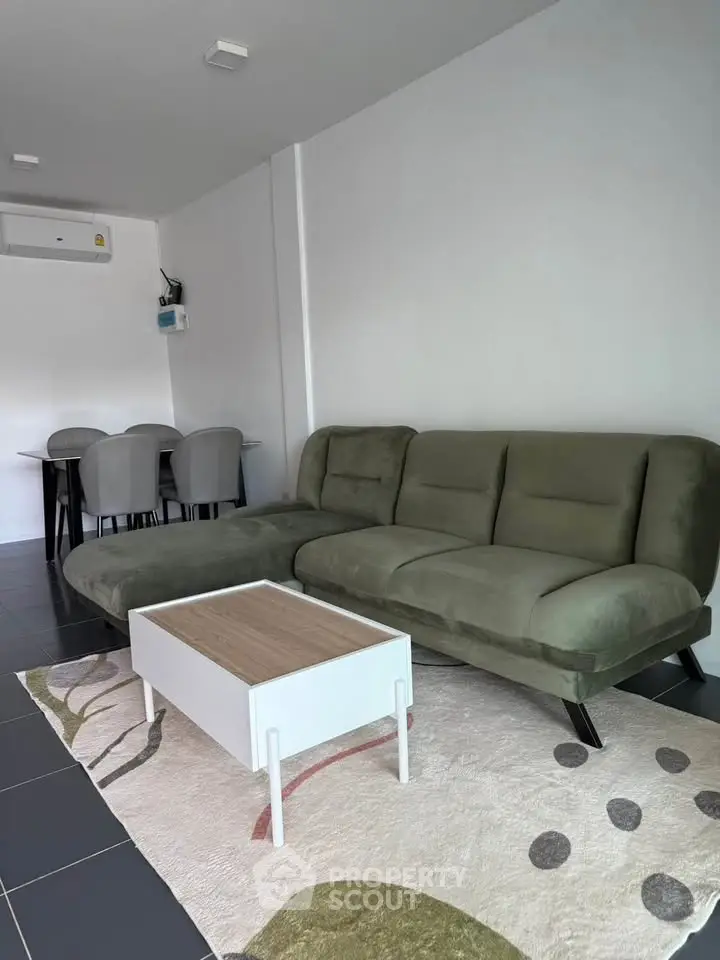 Modern living room with green sofa, stylish coffee table, and dining area in open layout.
