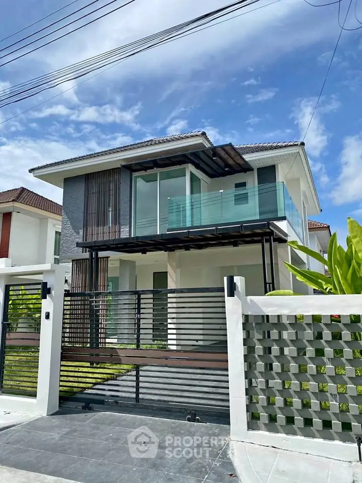 Modern two-story house with glass balcony and stylish facade under clear blue sky.