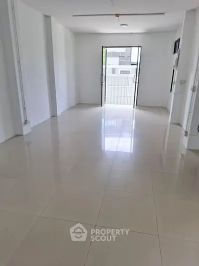 Spacious empty room with glossy tiled floor and large glass doors opening to balcony.