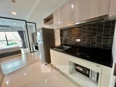 Modern kitchen with sleek appliances and open layout leading to a bright bedroom with balcony view.