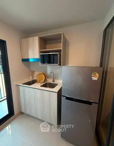 Modern compact kitchen with sleek fridge and microwave in a cozy apartment setting.