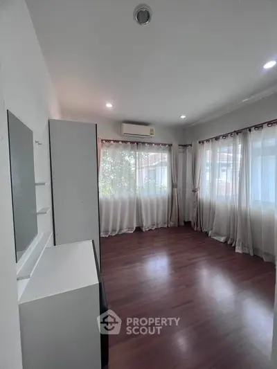 Spacious and bright room with large windows and wooden flooring, perfect for a cozy living space.