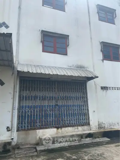 Industrial warehouse exterior with metal gate and red-framed windows.