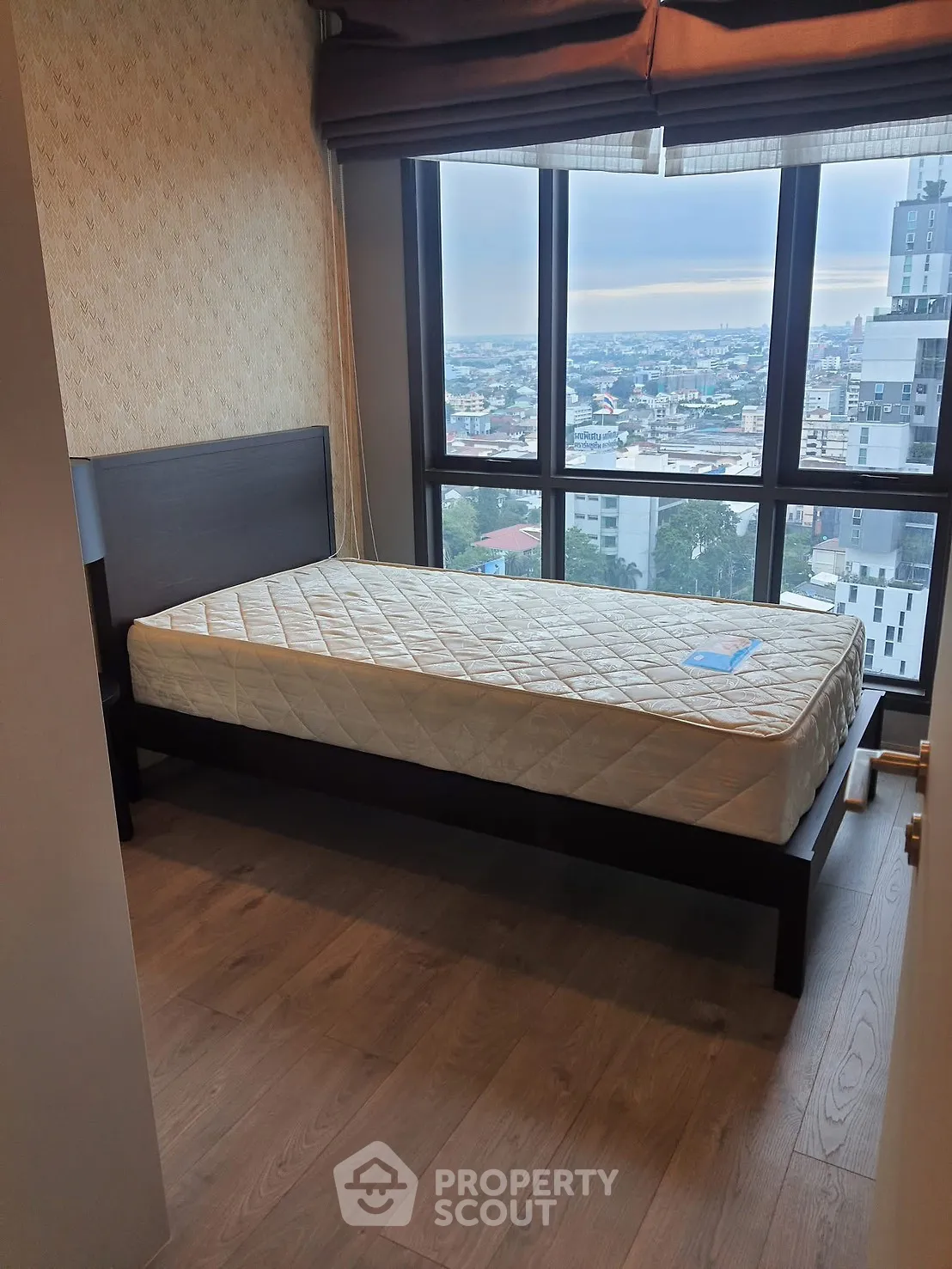 Cozy bedroom with single bed and stunning city view from large windows.