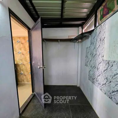 Compact storage room with open door and tiled floor, adjacent to a bathroom with floral tiles.