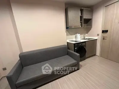 Modern compact living space with sofa and kitchenette featuring washing machine and storage cabinets.
