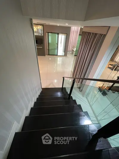 Elegant staircase leading to a modern living area with sleek glass railing and polished floors.