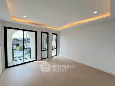 Spacious modern living room with large windows and balcony access, featuring elegant recessed lighting.