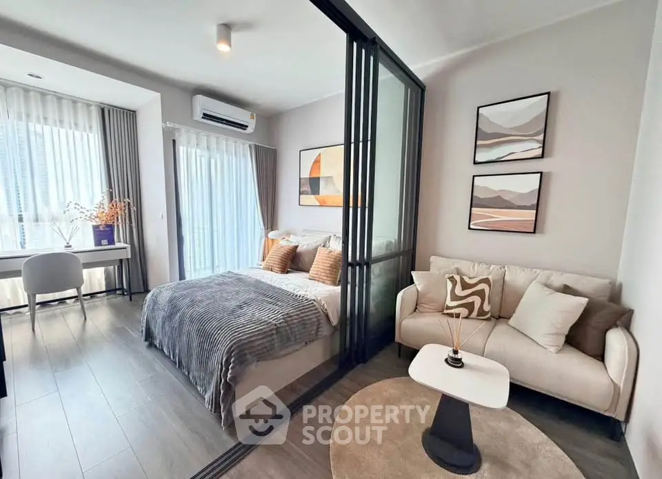 Modern bedroom with glass partition, cozy seating area, and stylish decor in a bright apartment.