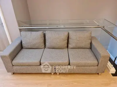 Modern gray sofa in stylish living room with glass railing and wooden floor.