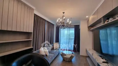 Elegant living room with modern decor and chandelier, featuring a large window with curtains and stylish furniture.