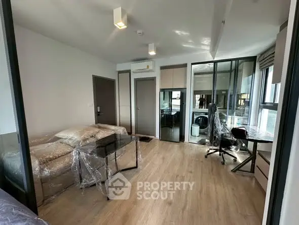 Modern living room with wooden flooring, glass partitions, and stylish furniture in a contemporary apartment.