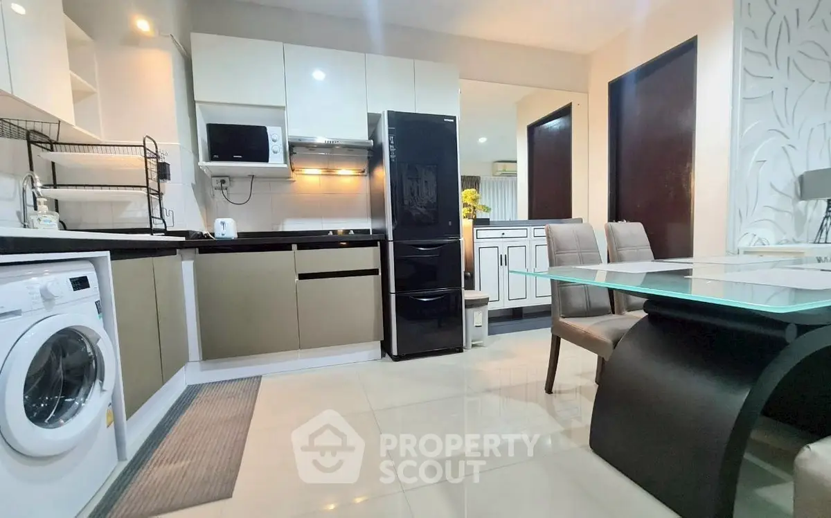 Modern kitchen with sleek appliances and dining area, featuring a washing machine and elegant decor.