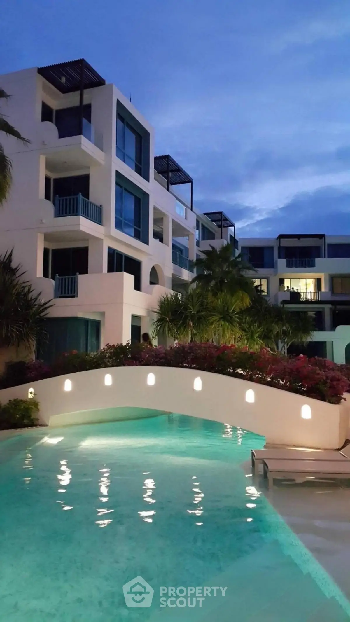 Luxurious modern apartment complex with stunning pool and lush landscaping at dusk.