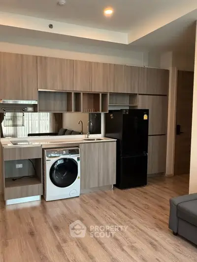 Modern kitchen with wooden cabinets, washing machine, and black fridge in stylish apartment.