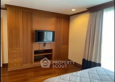 Elegant bedroom with built-in wooden wardrobe and mounted TV, featuring cozy ambiance and natural light.