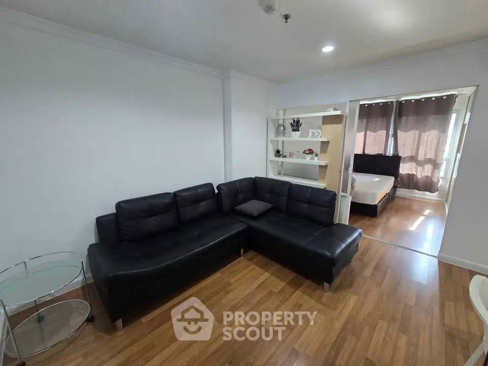 Modern living room with black leather sectional sofa and adjacent bedroom view.