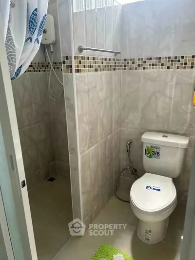 Compact bathroom with shower and toilet, featuring modern tile design and natural light.
