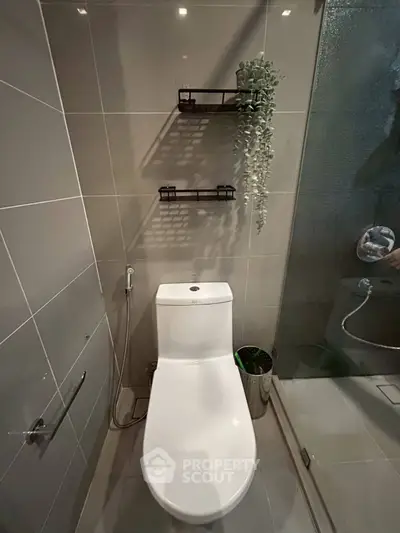 Modern bathroom with sleek toilet and glass shower enclosure, featuring stylish wall shelves and contemporary design.